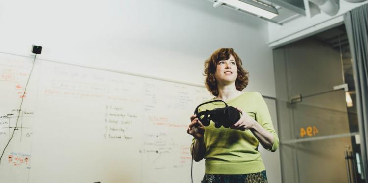 站立在教室的一个妇女看向一边，当拿着一对虚拟现实风镜时