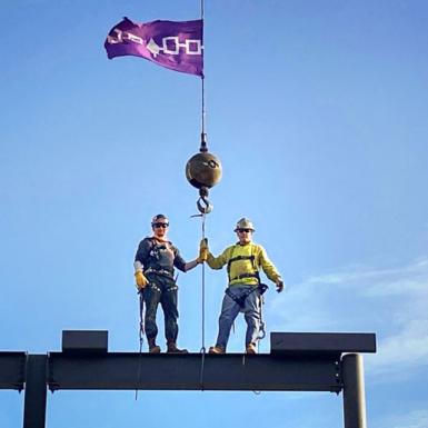 两名男子站在建筑脚手架上，举着一面紫色的旗帜