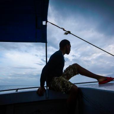 A person in silhouette at the front of a boat with a sail behind