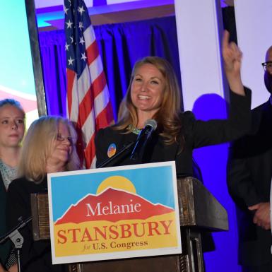 梅兰妮·斯坦斯伯里和支持者站在讲台后面庆祝，讲台上有她的竞选标志